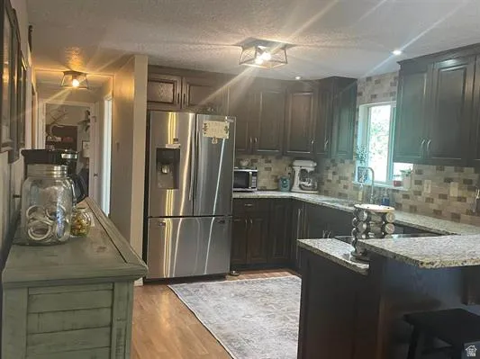 Dark wood-finish cabinetry, granite-style countertops, stainless steel refrigerator, tile backsplash, and wood-finish flooring