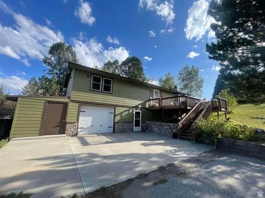 Multi-level exterior with olive green siding, an attached garage, and a wood deck