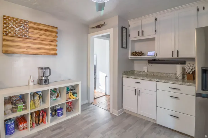 White cabinetry, light-toned countertops, stainless steel refrigerator, and wood-finish flooring