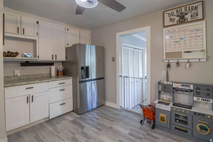 White cabinetry with dark hardware, stainless steel refrigerator, light gray wood-finish flooring, and light-toned countertops