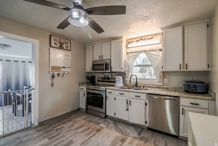 Well-appointed kitchen featuring white cabinetry with dark hardware, stainless steel appliances, granite-style countertops, and wood-finish flooring