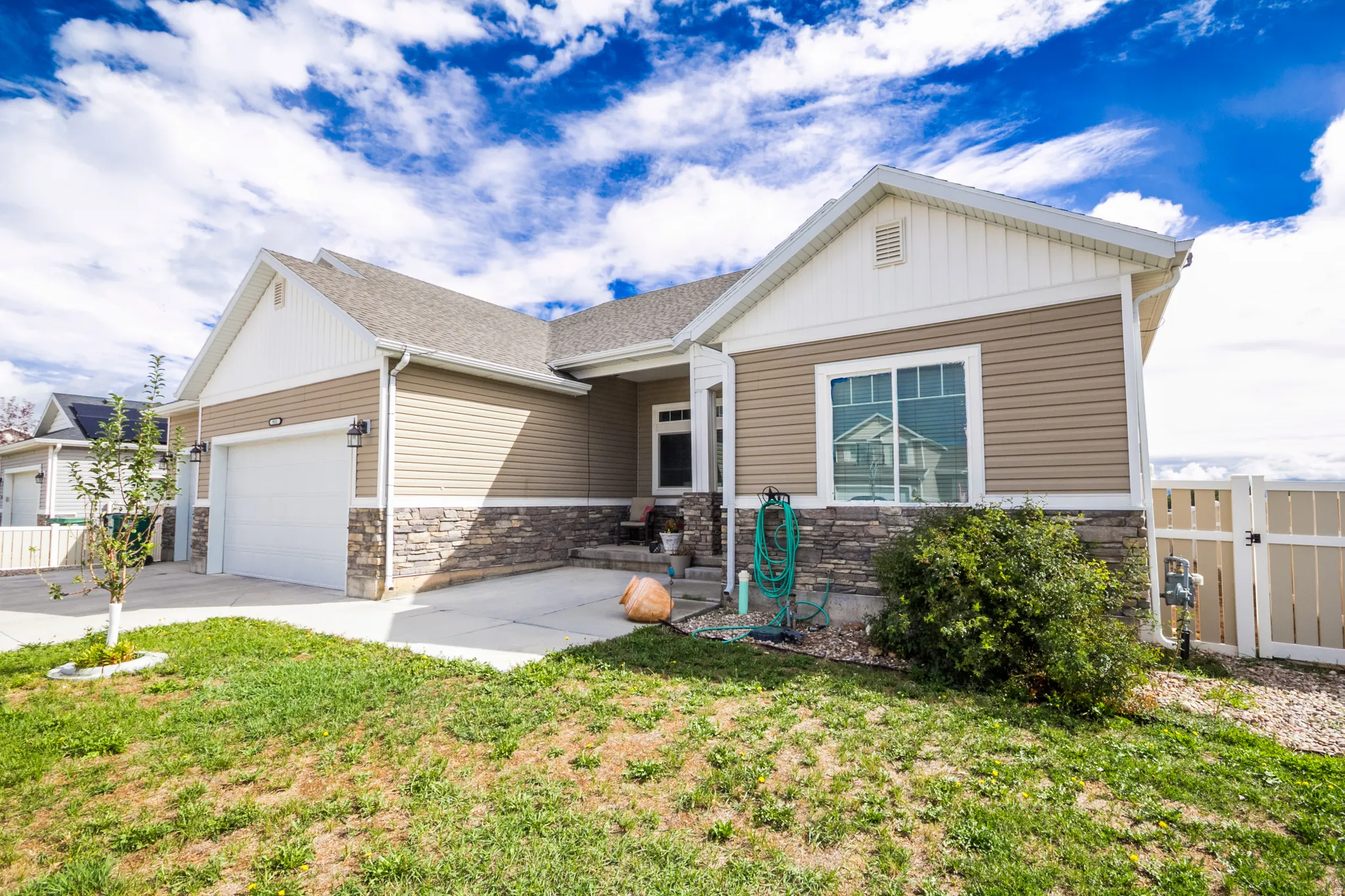 Exterior featuring horizontal siding, stone veneer accents, an attached garage, a paved driveway, and a fenced yard