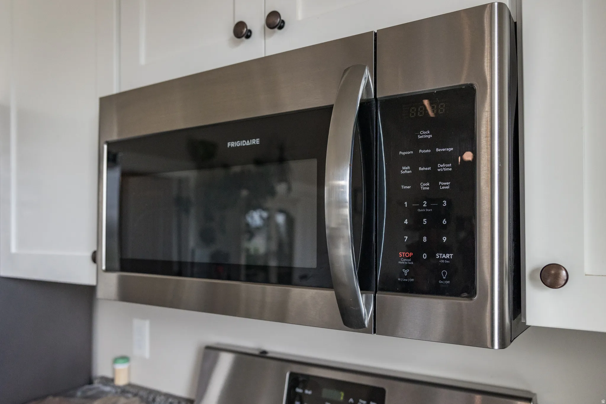 Stainless steel microwave oven with digital controls and a large handle, integrated into white upper cabinetry with dark bronze hardware