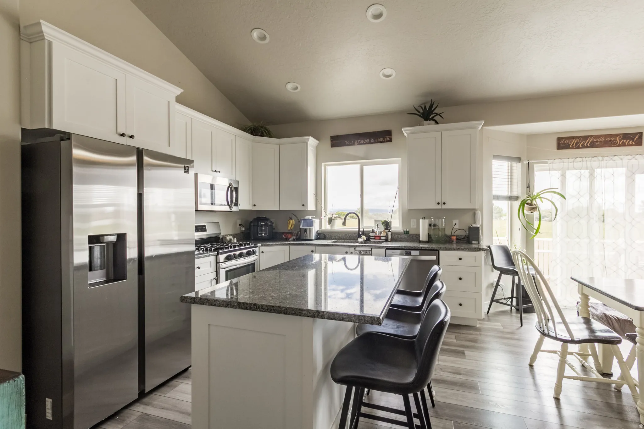 Kitchen featuring white cabinetry, stainless steel appliances, a center island with a granite-style countertop, and wood-finish flooring