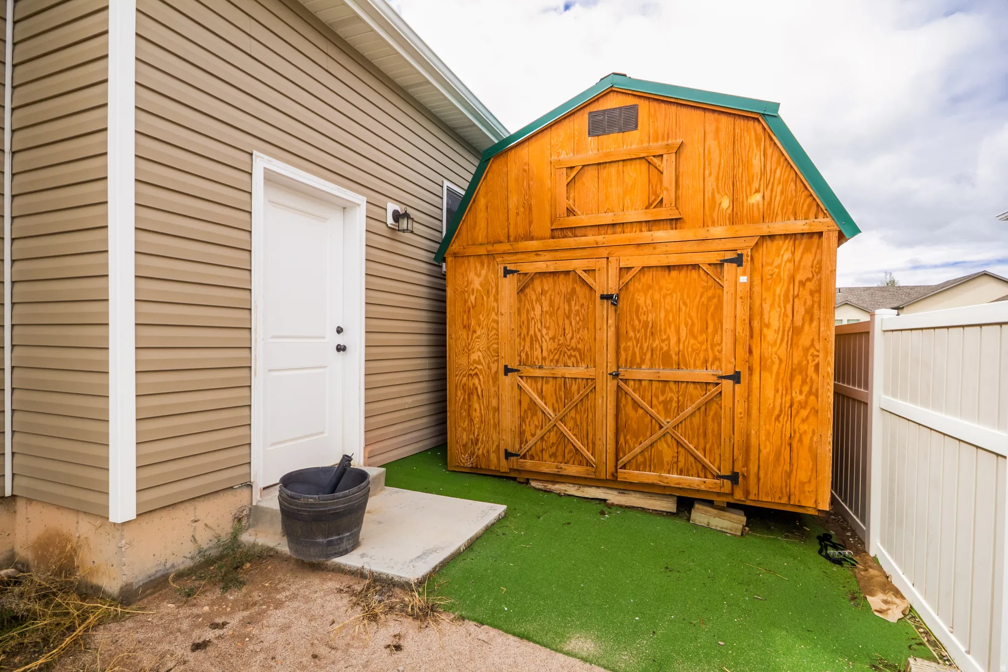 Exterior features include a wooden storage shed with a green roof, a white privacy fence, and a concrete pad
