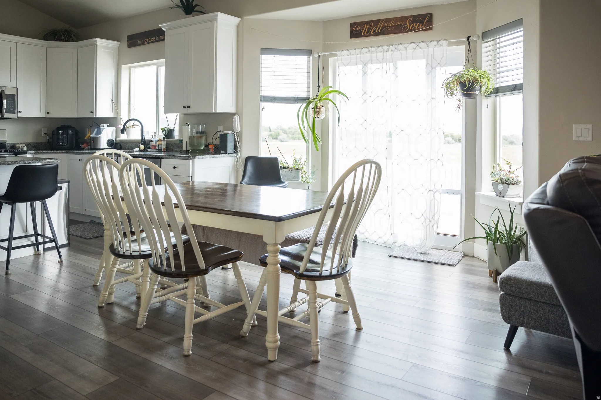 Light wood-finish flooring extending into the kitchen, white cabinetry with dark hardware, dark countertops, and a sliding glass door with transom window