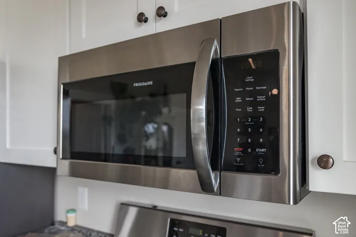 Stainless steel microwave oven with digital controls and a large handle, integrated into white upper cabinetry with dark bronze hardware