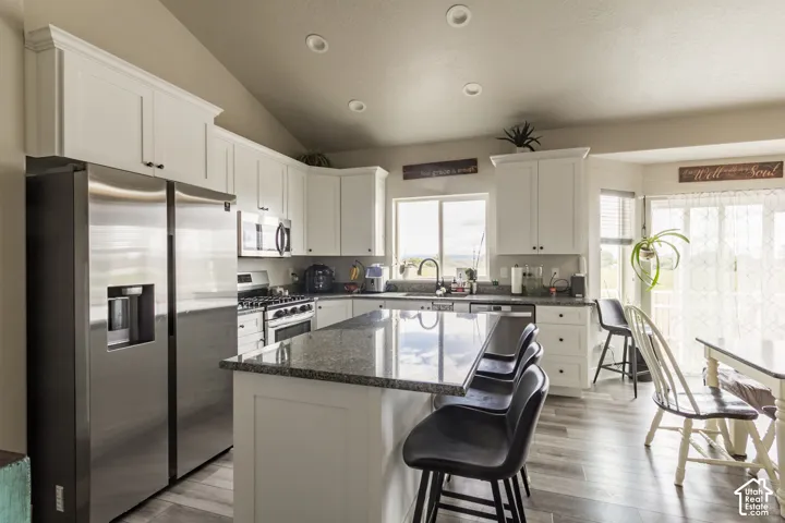 Kitchen featuring white cabinetry, stainless steel appliances, a center island with a granite-style countertop, and wood-finish flooring