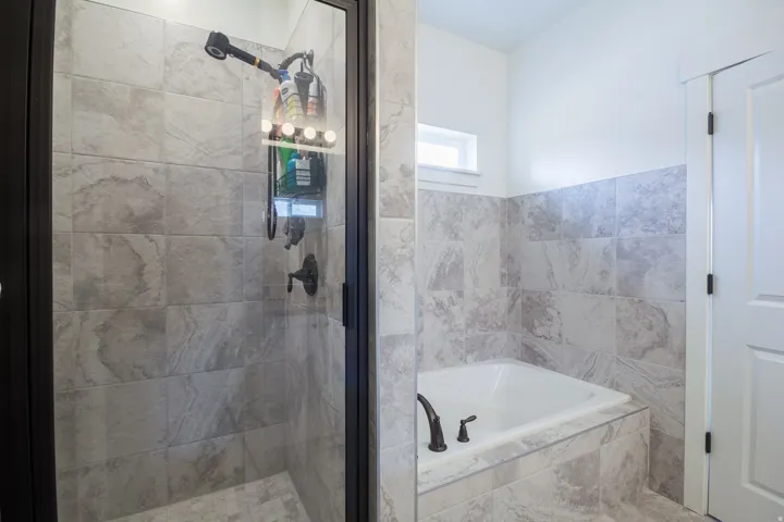 Tiled shower enclosure with a dark-framed glass door, featuring a built-in bathtub with dark bronze fixtures