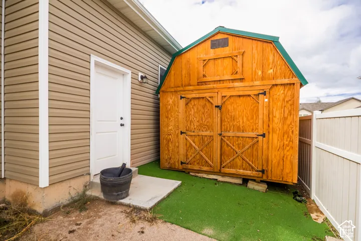 Exterior features include a wooden storage shed with a green roof, a white privacy fence, and a concrete pad