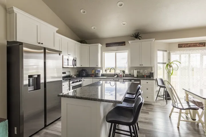 Kitchen featuring white cabinetry, stainless steel appliances, a center island with a granite-style countertop, and wood-finish flooring