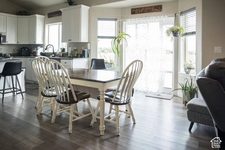 Light wood-finish flooring extending into the kitchen, white cabinetry with dark hardware, dark countertops, and a sliding glass door with transom window