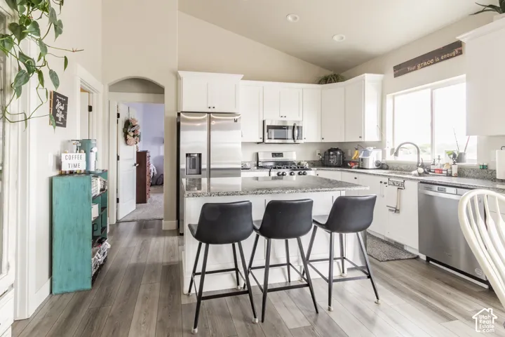 Kitchen featuring white cabinetry, granite-finish countertops, stainless steel appliances, and wood-finish flooring