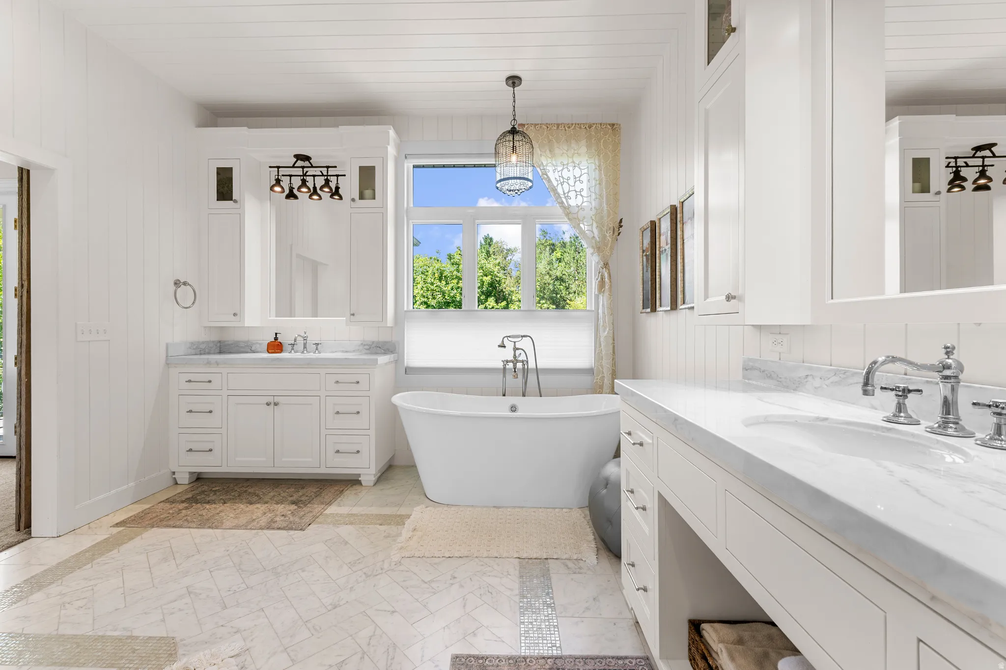 Freestanding bathtub with floor-mounted faucet, dual vanity with undermount sinks, stone countertops, and herringbone tile flooring