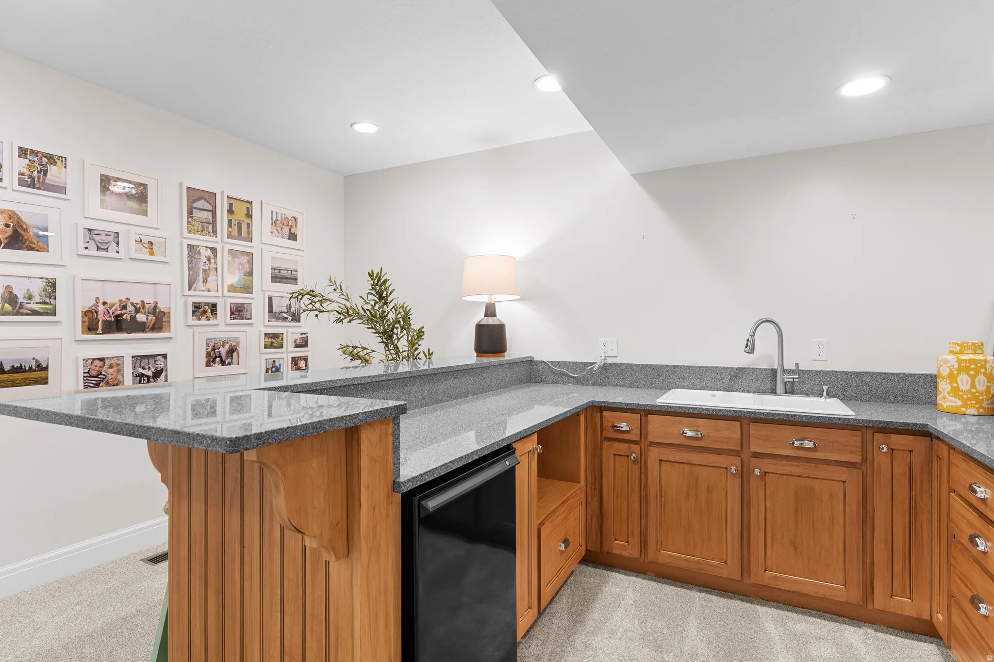 Wet bar featuring light wood-finish cabinetry, gray stone countertops, and an undermount sink with a gooseneck faucet
