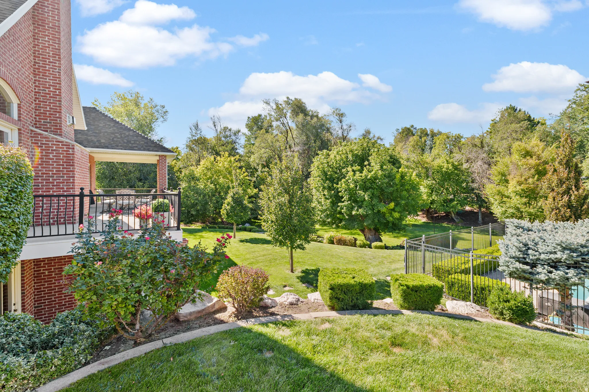Expansive backyard featuring a manicured lawn, established landscaping, and a covered balcony with a black railing