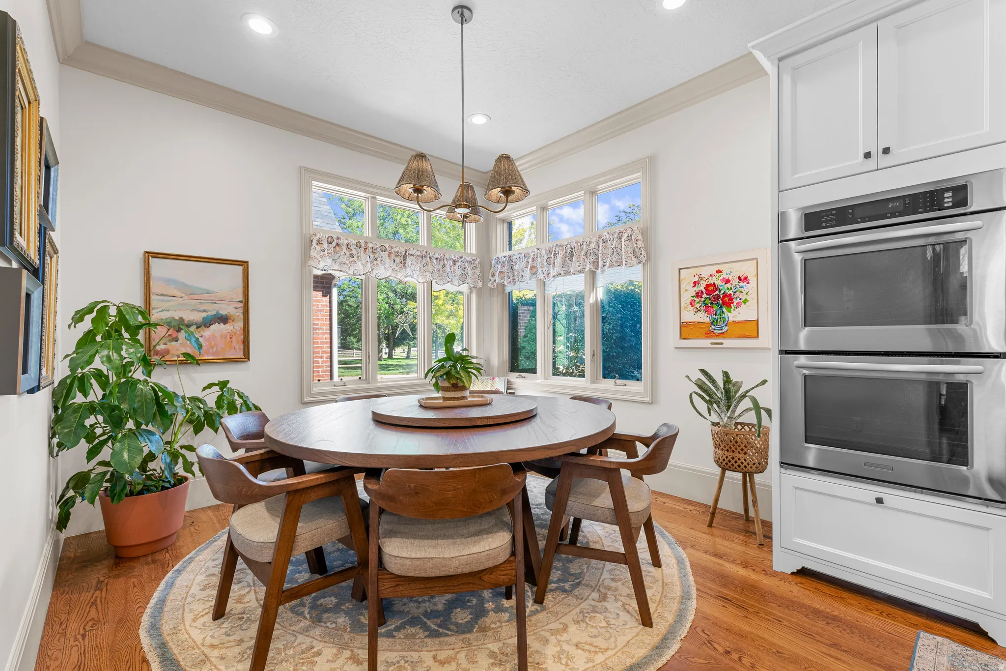 Built-in stainless steel double ovens, white cabinetry, wood-finish flooring, recessed lighting, and a multi-pane window configuration