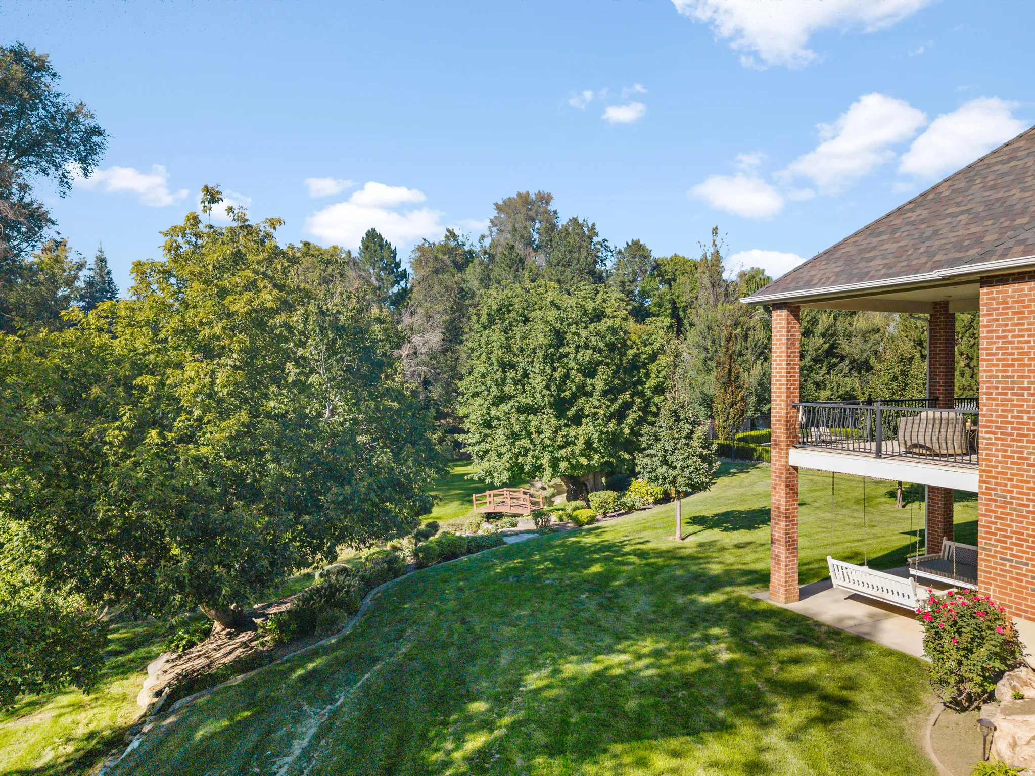 Brick exterior with covered patio, second-story balcony with black railing, and expansive green lawn