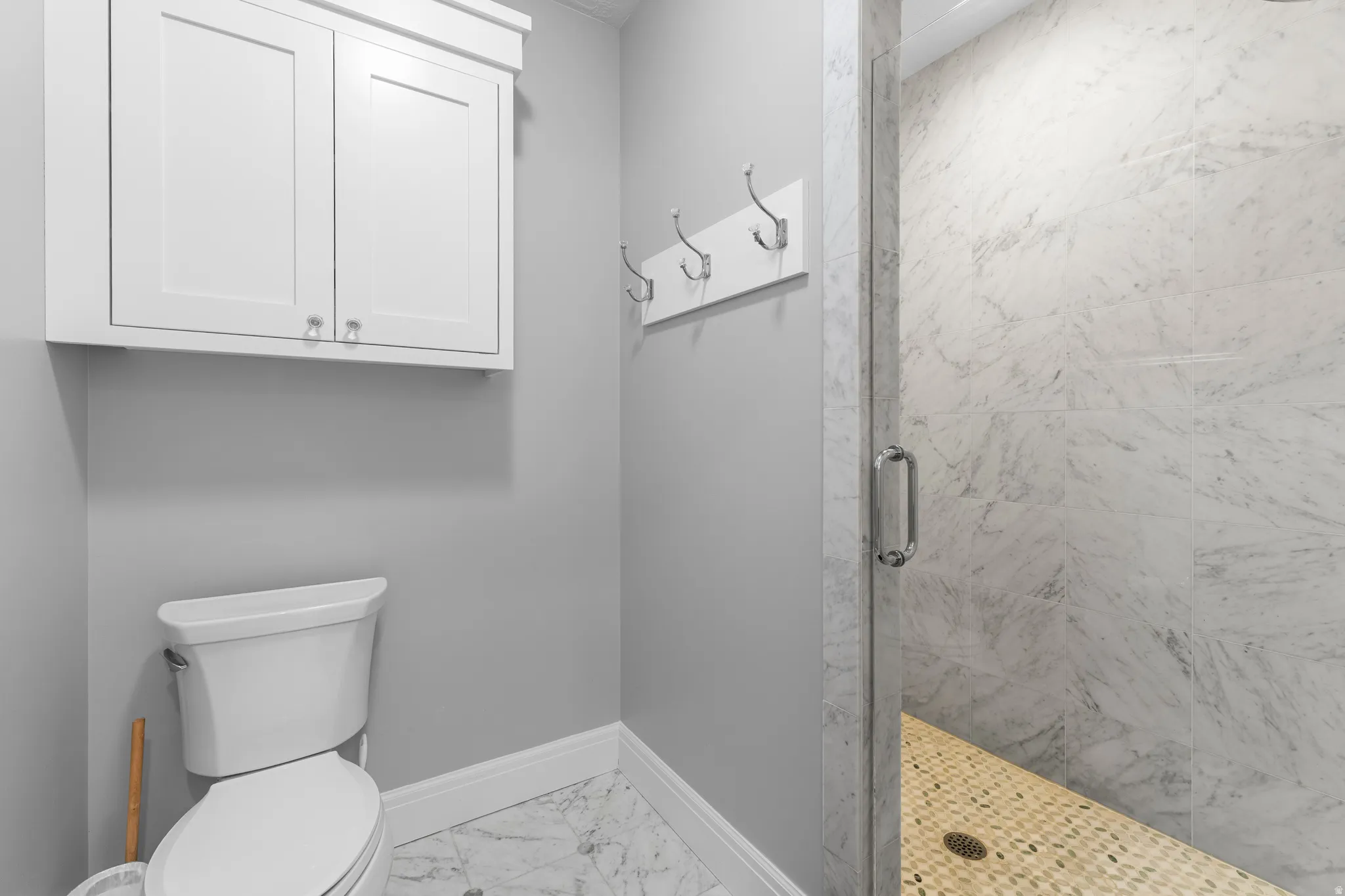 Walk-in shower with natural stone tile, glass enclosure with chrome hardware, and pebble flooring