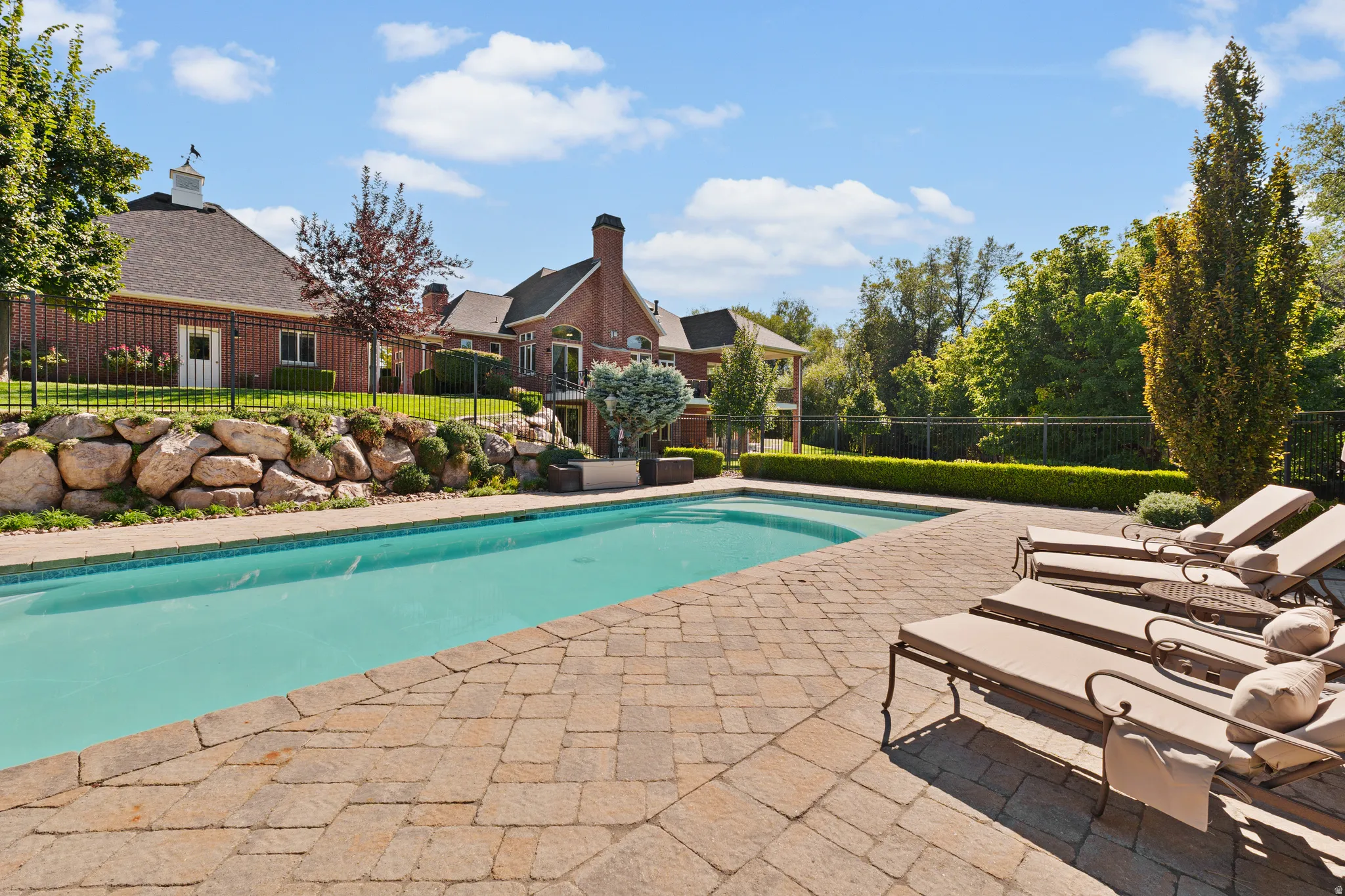 Outdoor pool, expansive paver patio, stone retaining wall, and mature landscaping