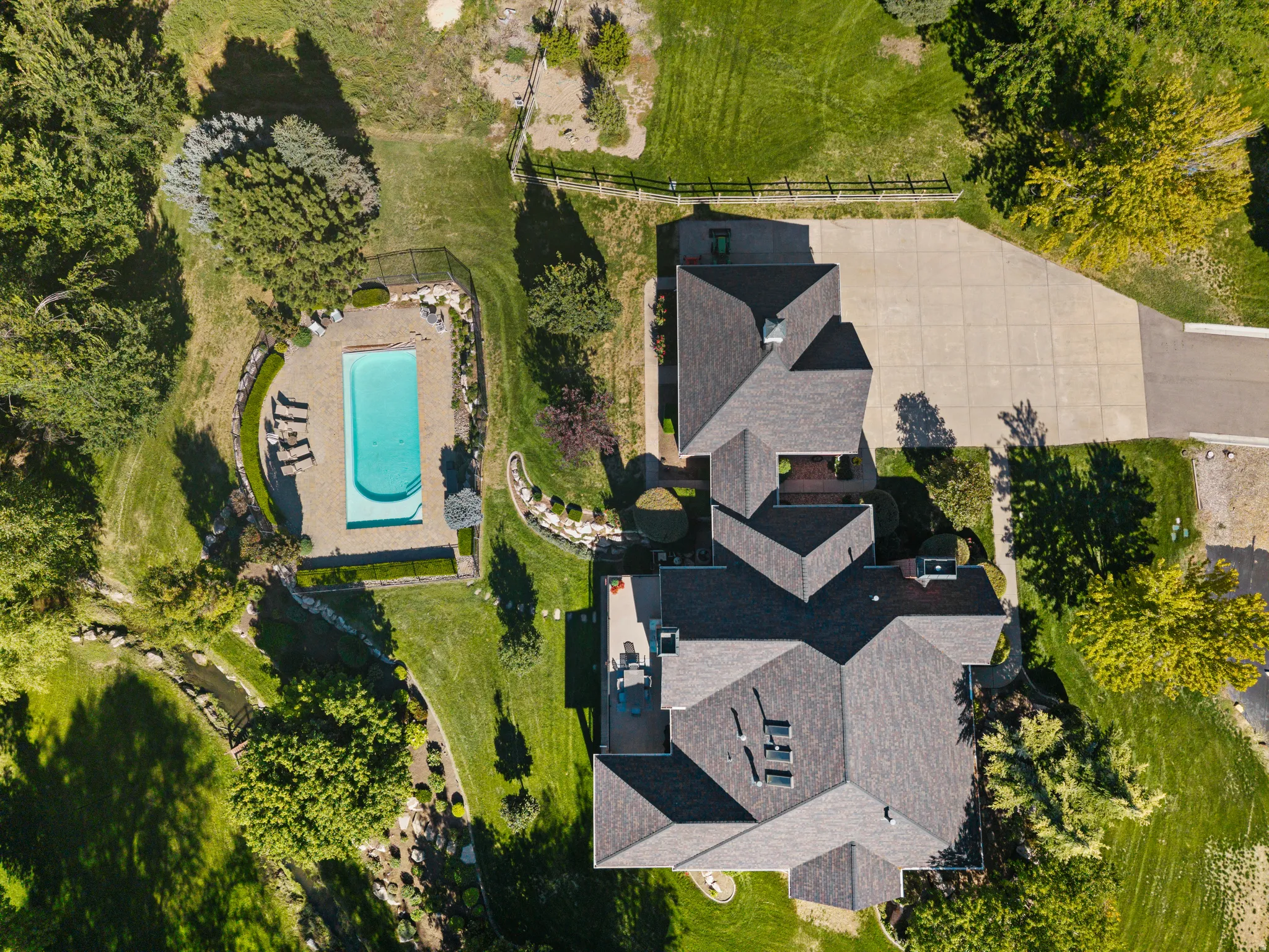 Expansive property featuring a multi-level residence, a rectangular swimming pool with surrounding patio, extensive paved driveway, and mature landscaping