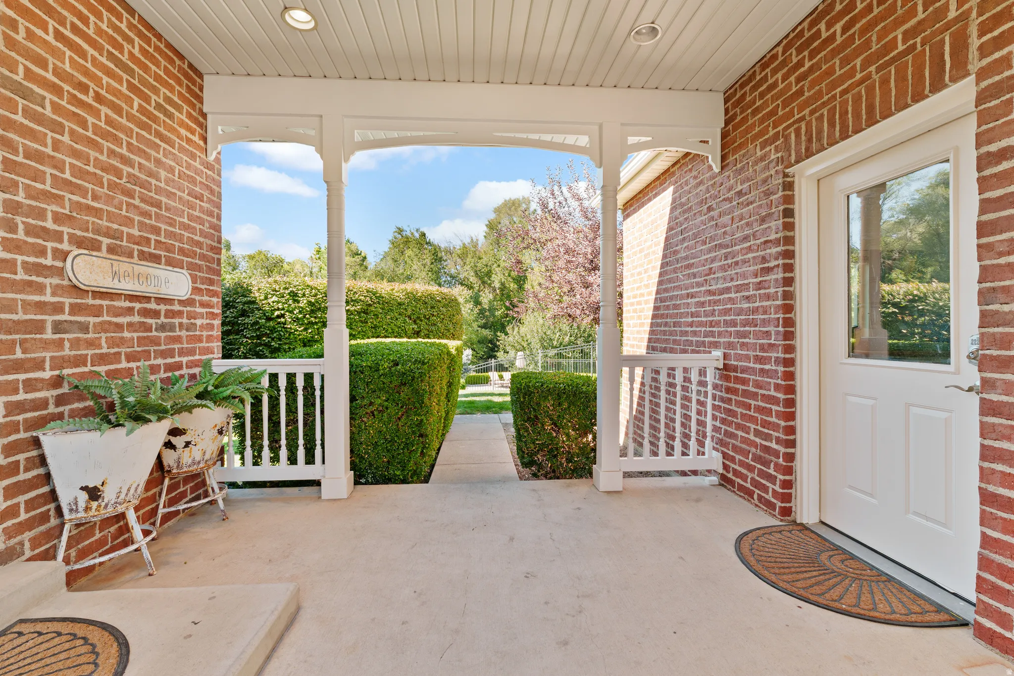 Covered entry with recessed lighting, brick exterior, white balustrade, and a glass-paneled entry door