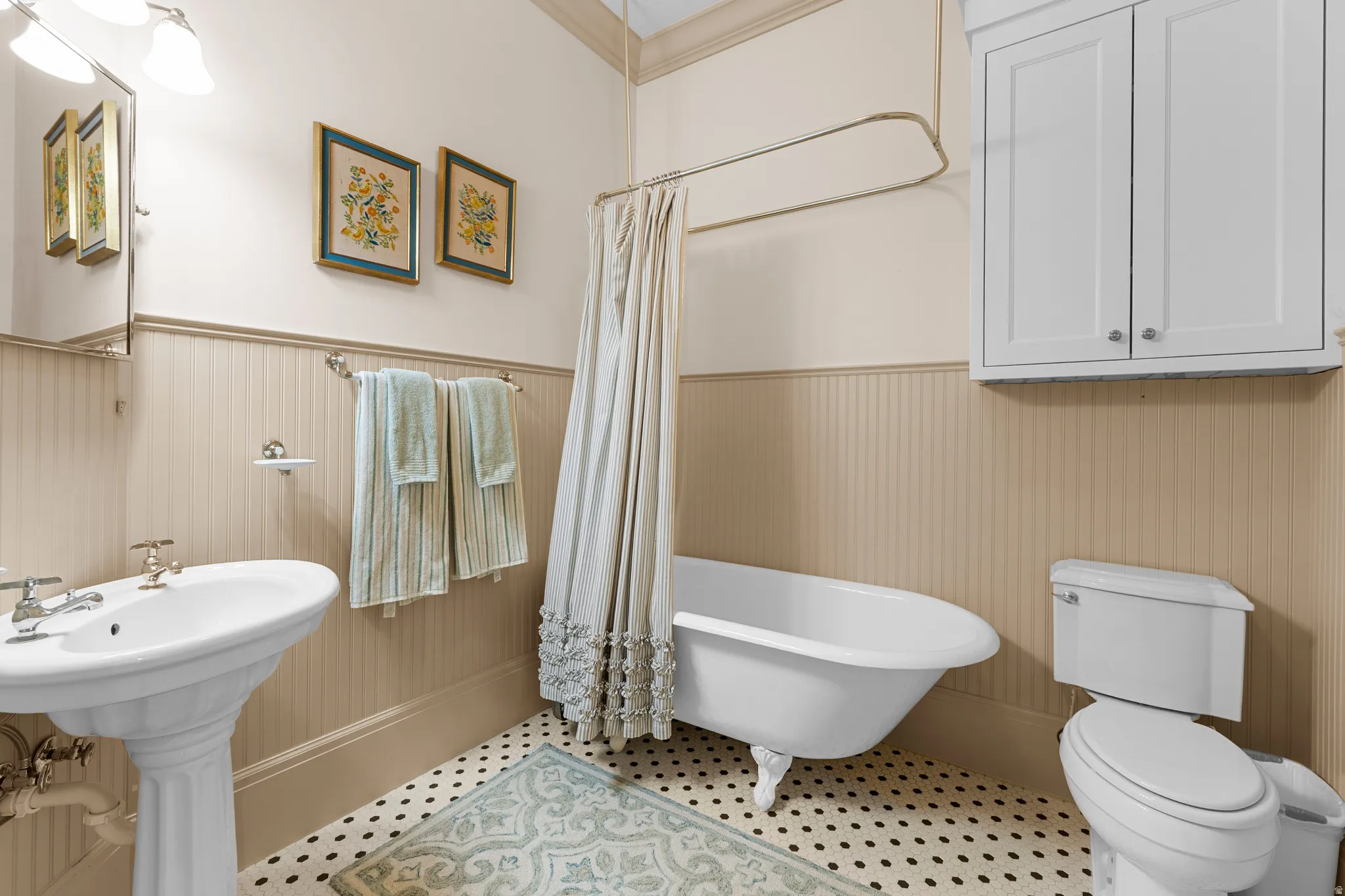 Pedestal sink, beadboard wainscoting, traditional clawfoot bathtub, white wall-mounted cabinetry, and black and white mosaic tile flooring