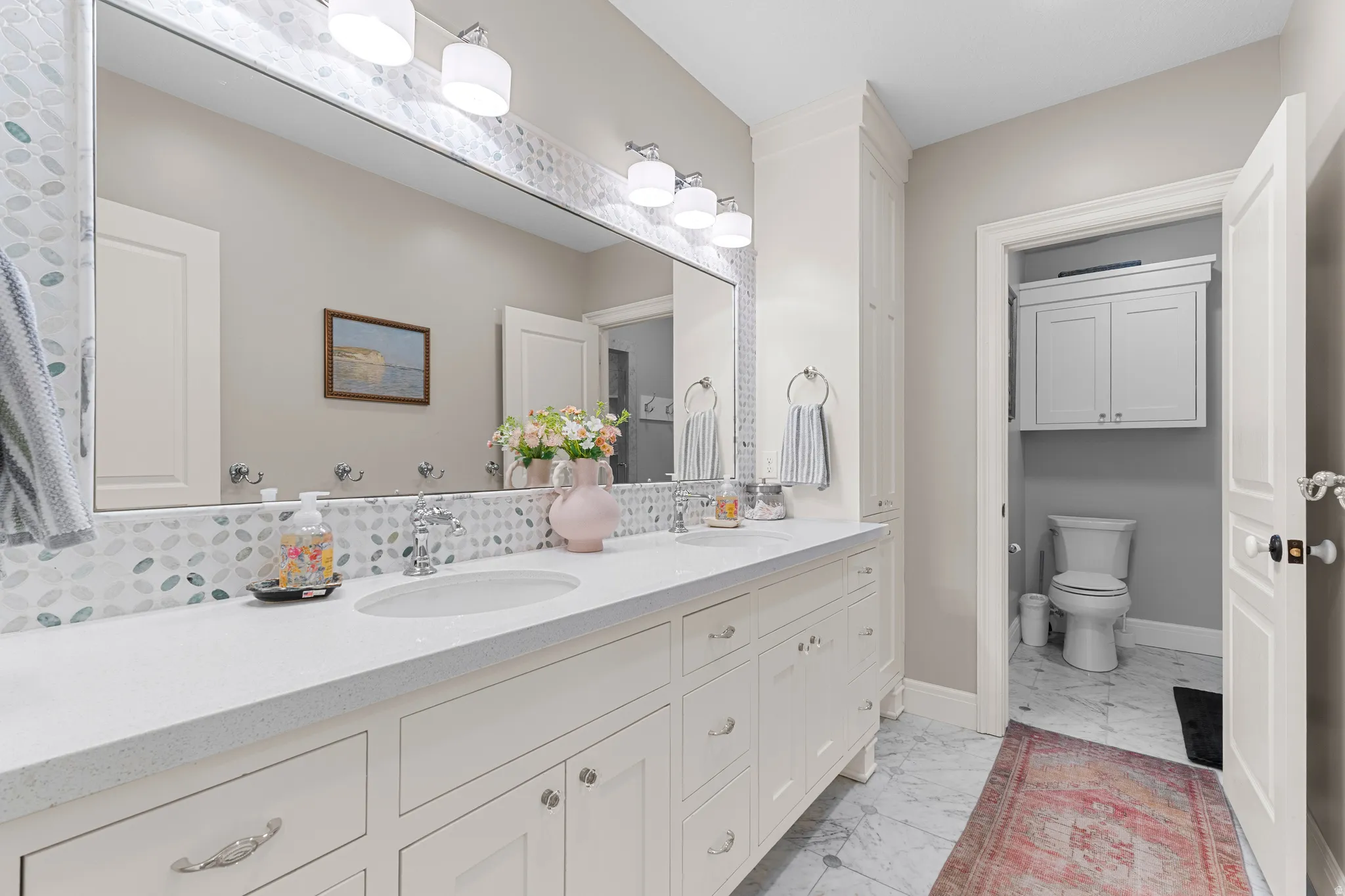Dual undermount sinks with chrome fixtures, an expansive vanity with white shaker-style cabinetry, and a full-width mirror