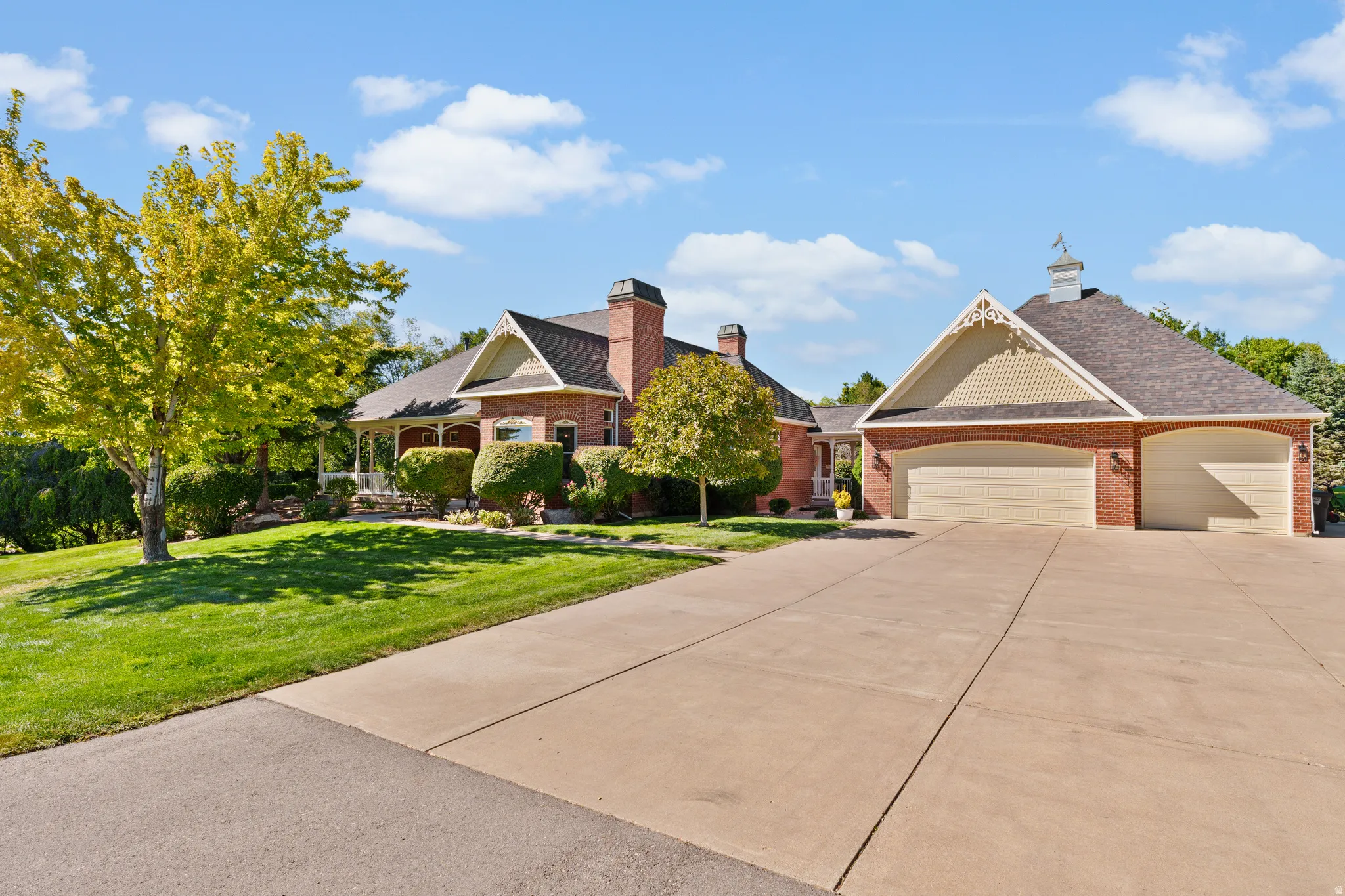 Brick exterior with shingled roof, attached garage, extended driveway, and mature landscaping