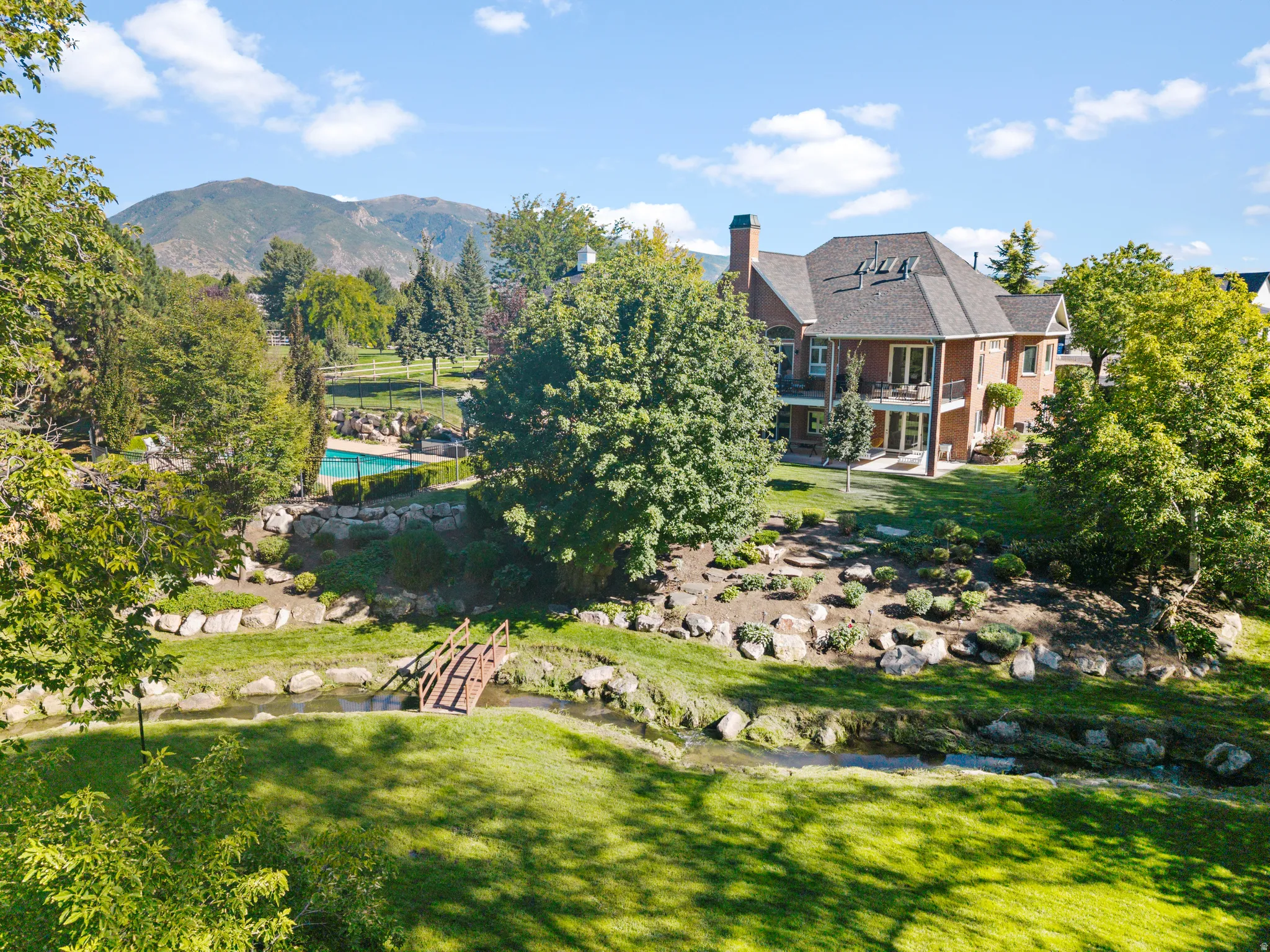 Brick exterior residence with multi-level balconies, expansive green space, and a swimming pool
