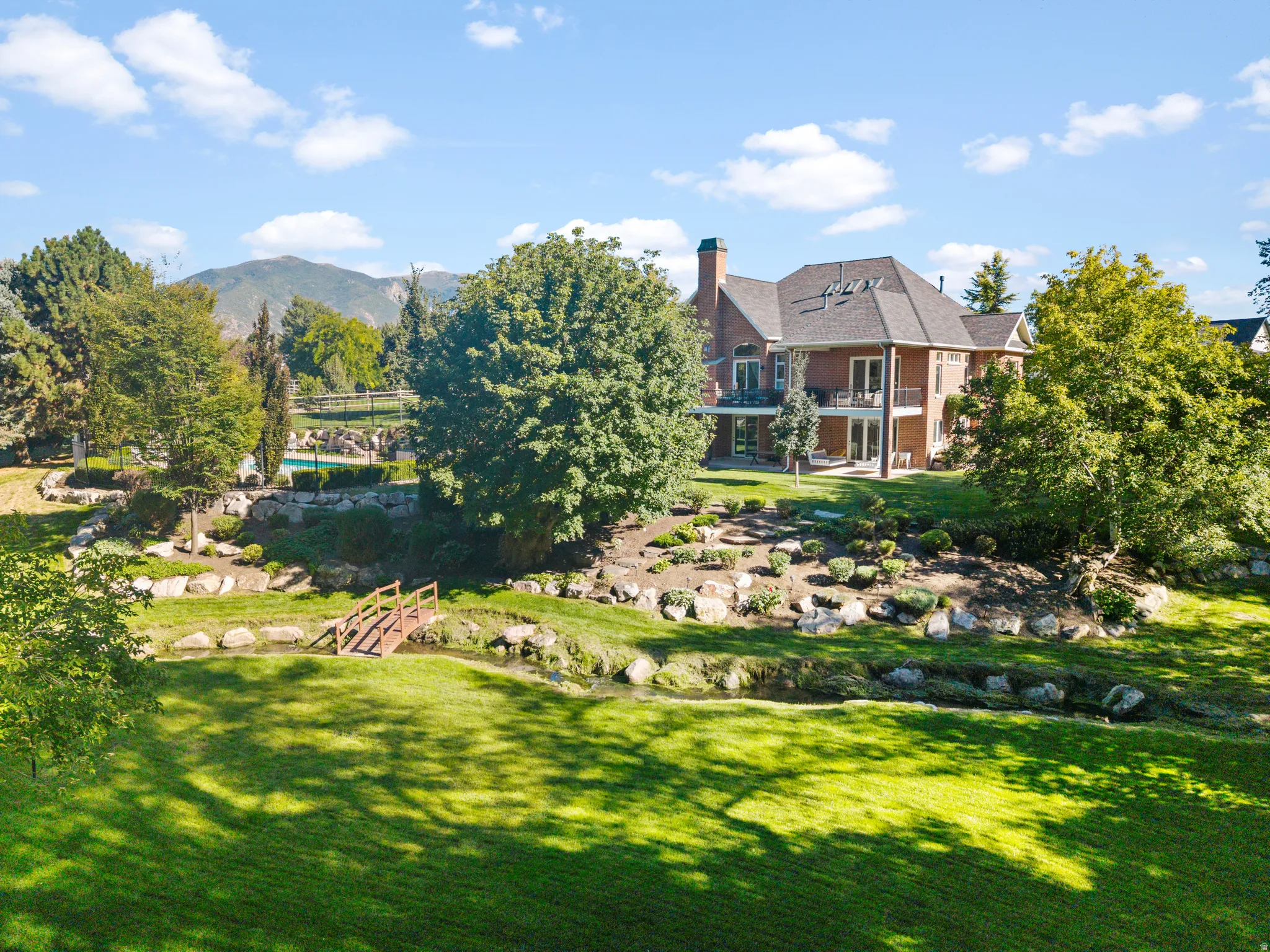 Brick exterior with multiple balconies, expansive green lawn, mature trees, and a visible swimming pool