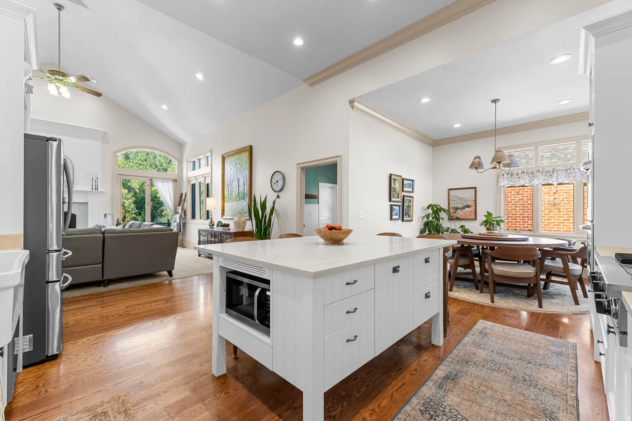 White kitchen island with stone countertop, wood-finish flooring, vaulted ceilings, and recessed lighting