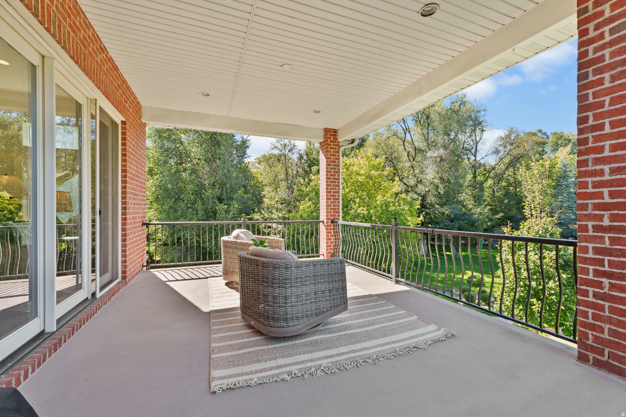 Expansive outdoor covered balcony featuring a brick exterior, white sliding glass doors, white paneled ceiling, and black wrought iron railing