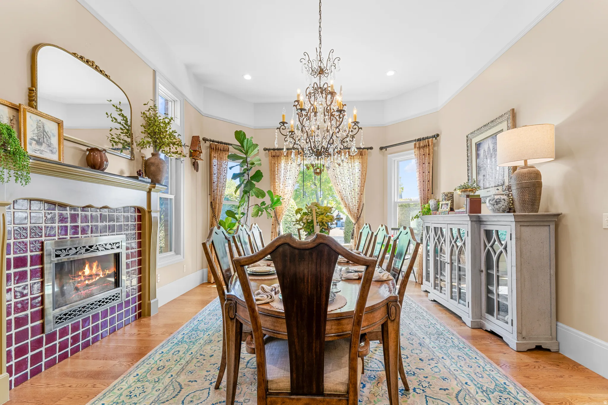 Wood-finish flooring, tiled fireplace surround, ornate chandelier, bay window, and crown molding