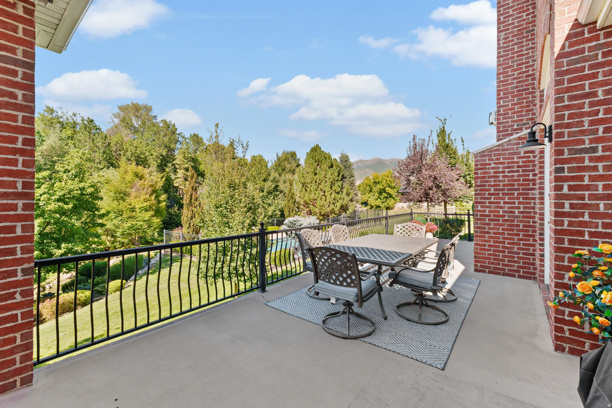 Expansive outdoor patio with concrete flooring, black metal railings, and a brick exterior wall