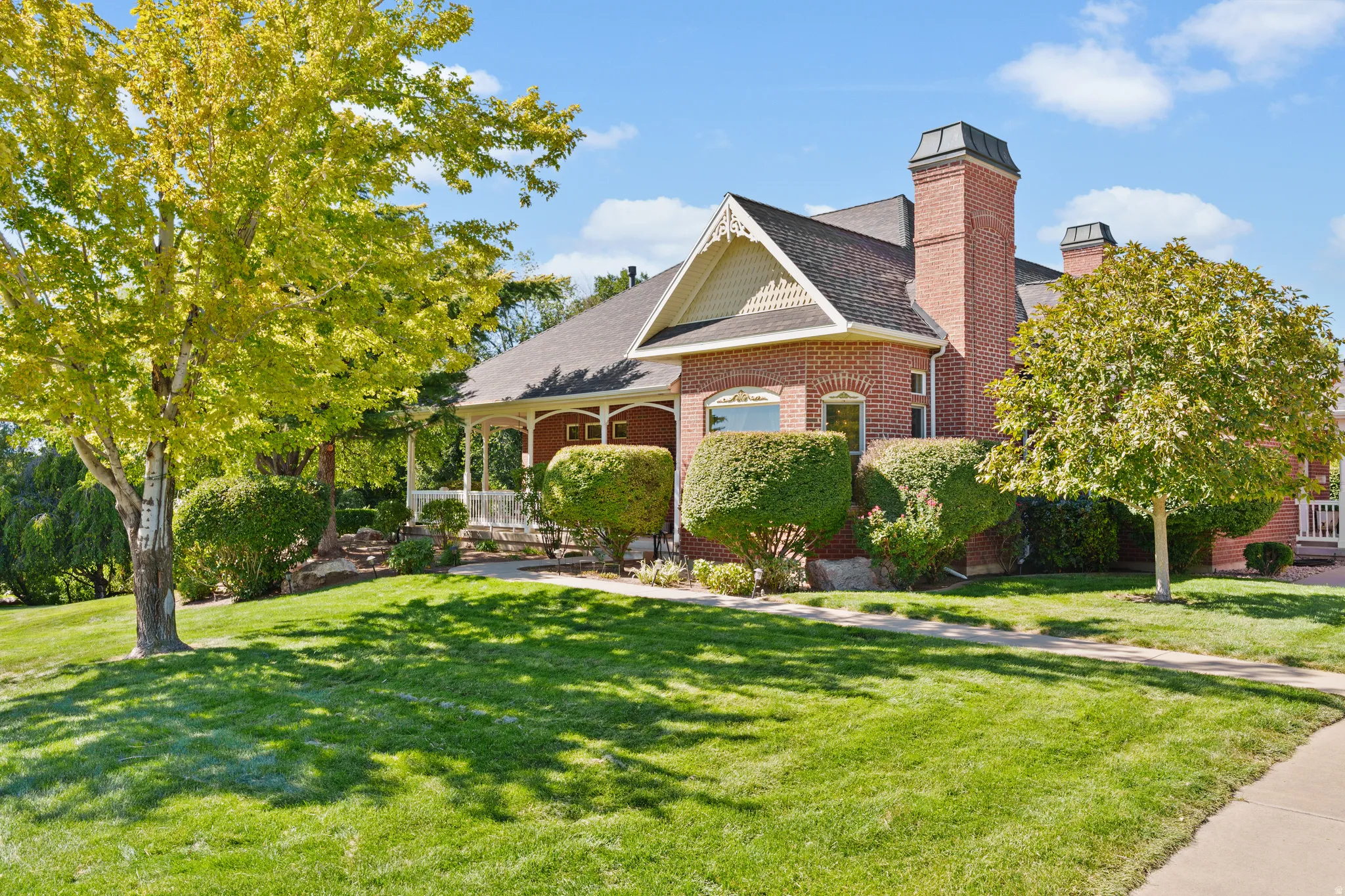 Brick exterior with a covered porch, gabled roofline, multiple chimneys, and mature landscaping