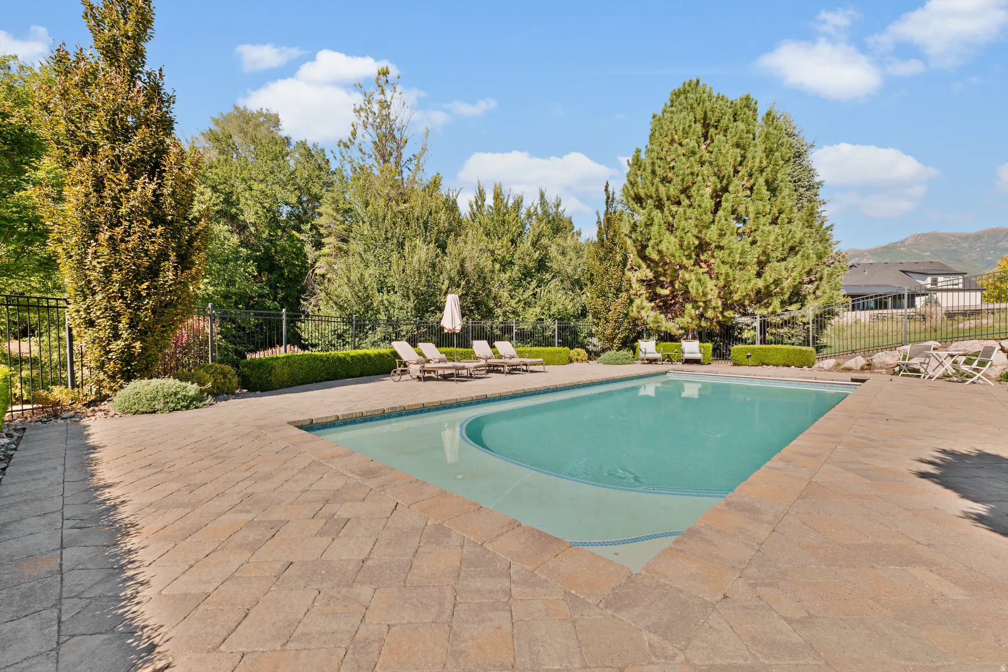 Expansive outdoor space featuring a rectangular swimming pool with integrated seating, surrounded by a paver patio