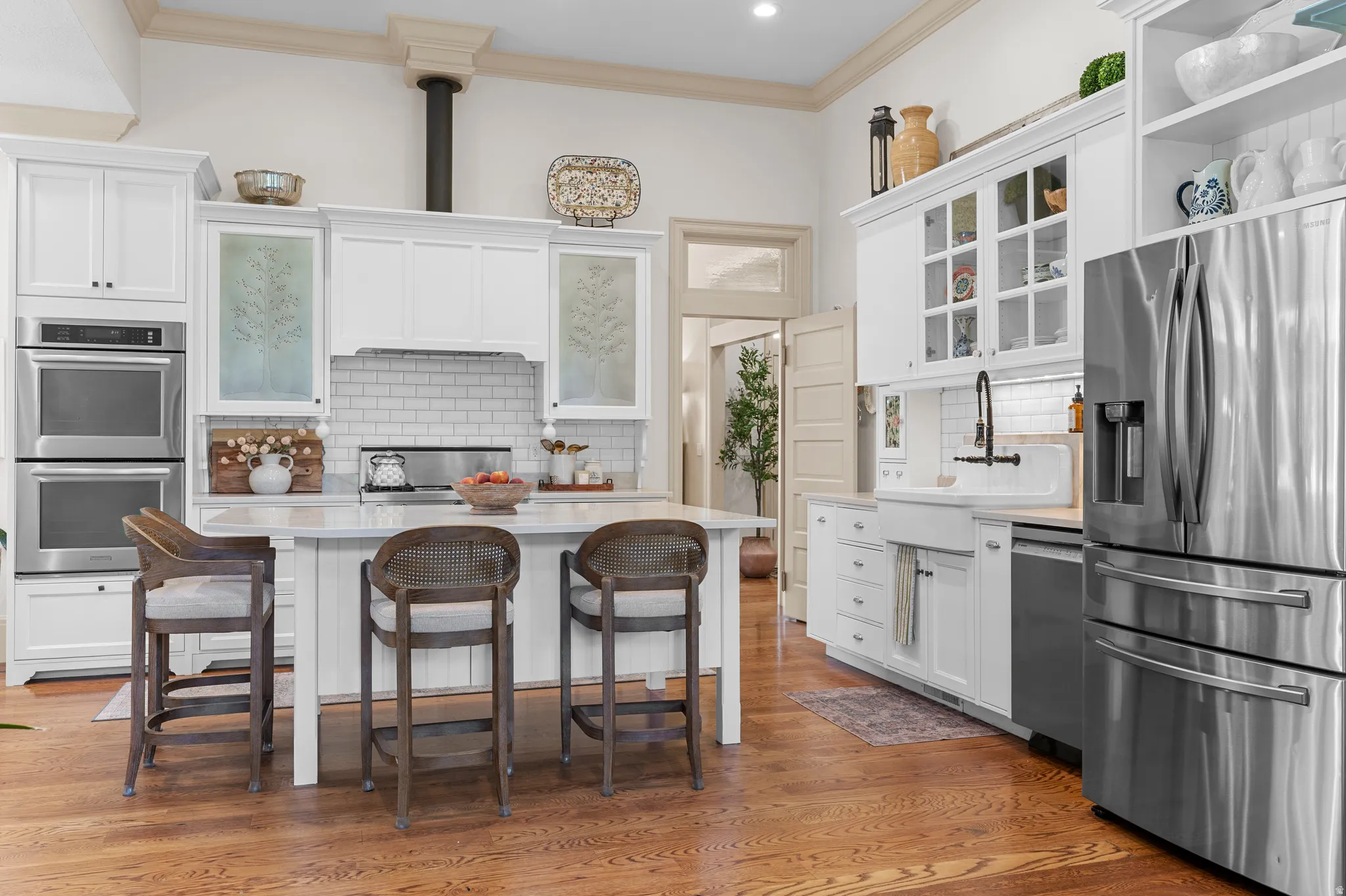 Gleaming wood-finish flooring, white cabinetry, integrated double ovens, a center island, and a farmhouse sink with a black-finish faucet