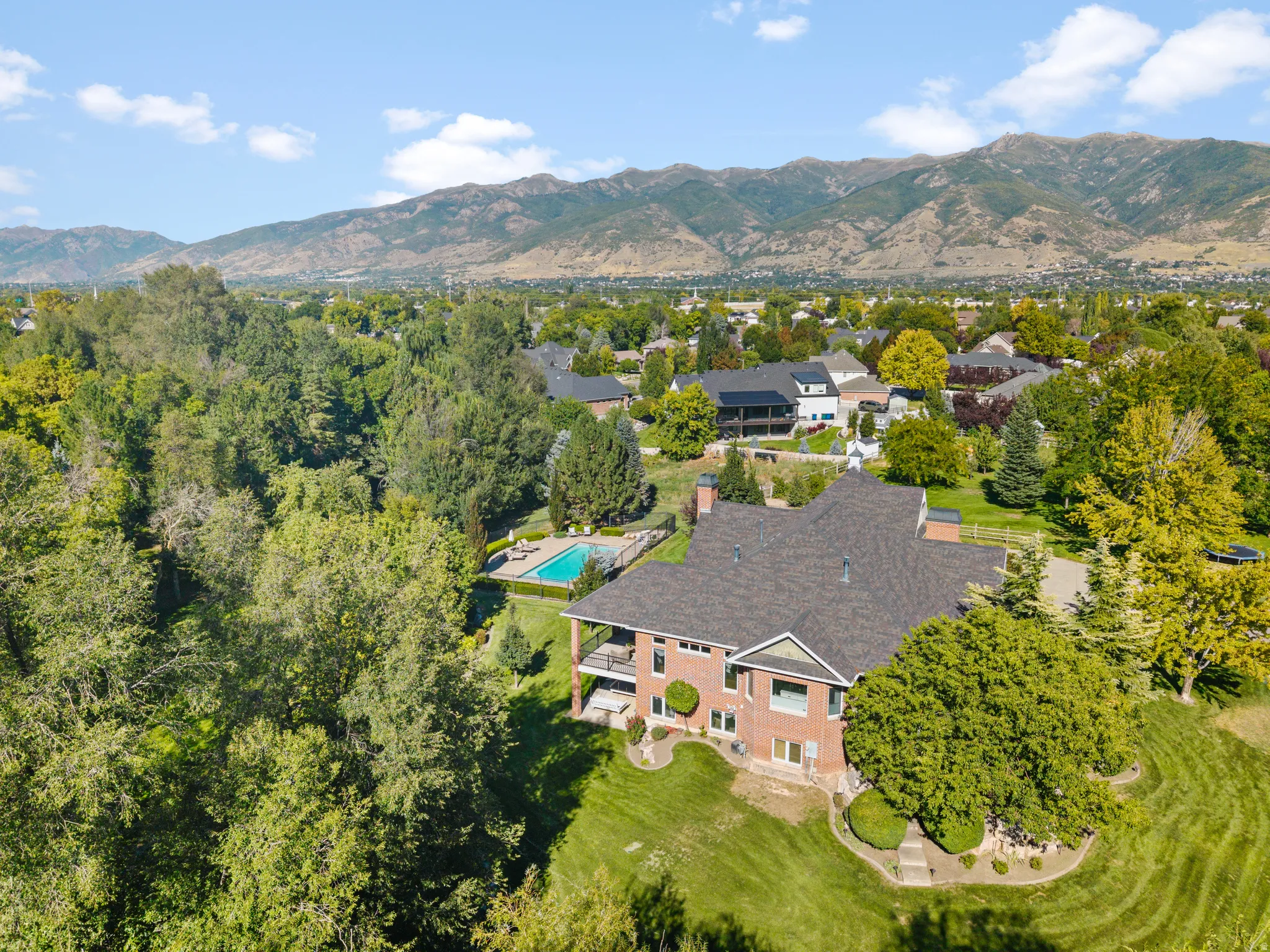 Brick exterior, multi-level structure, covered patio, rear swimming pool, and mountain backdrop