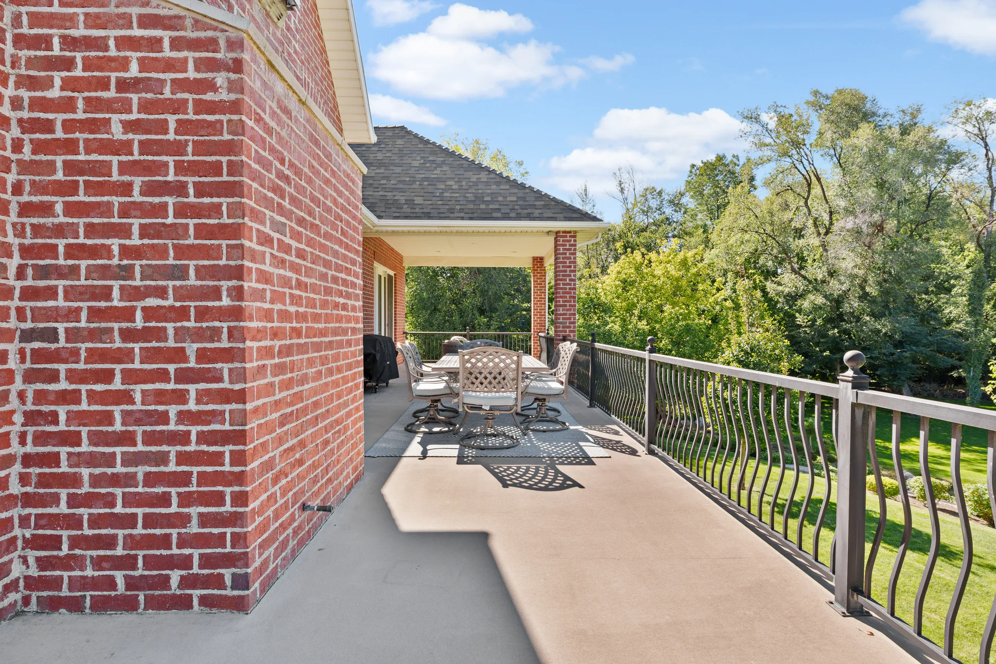 Expansive outdoor patio with a covered section, brick exterior, and decorative wrought iron railing