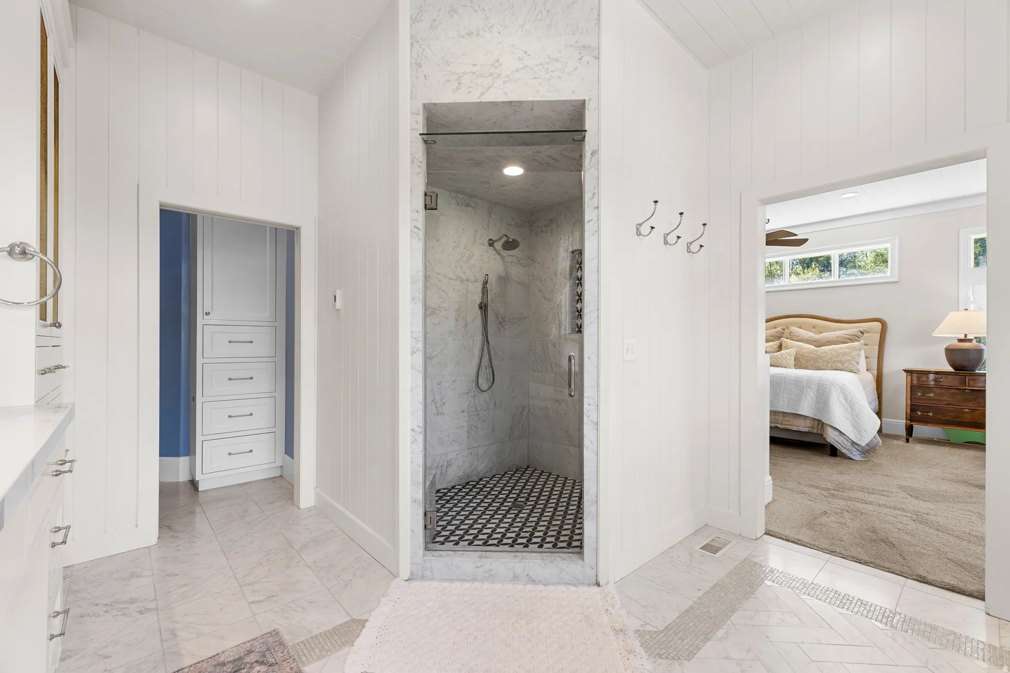 Walk-in shower with glass enclosure, custom tile flooring, and marble-finish wall paneling