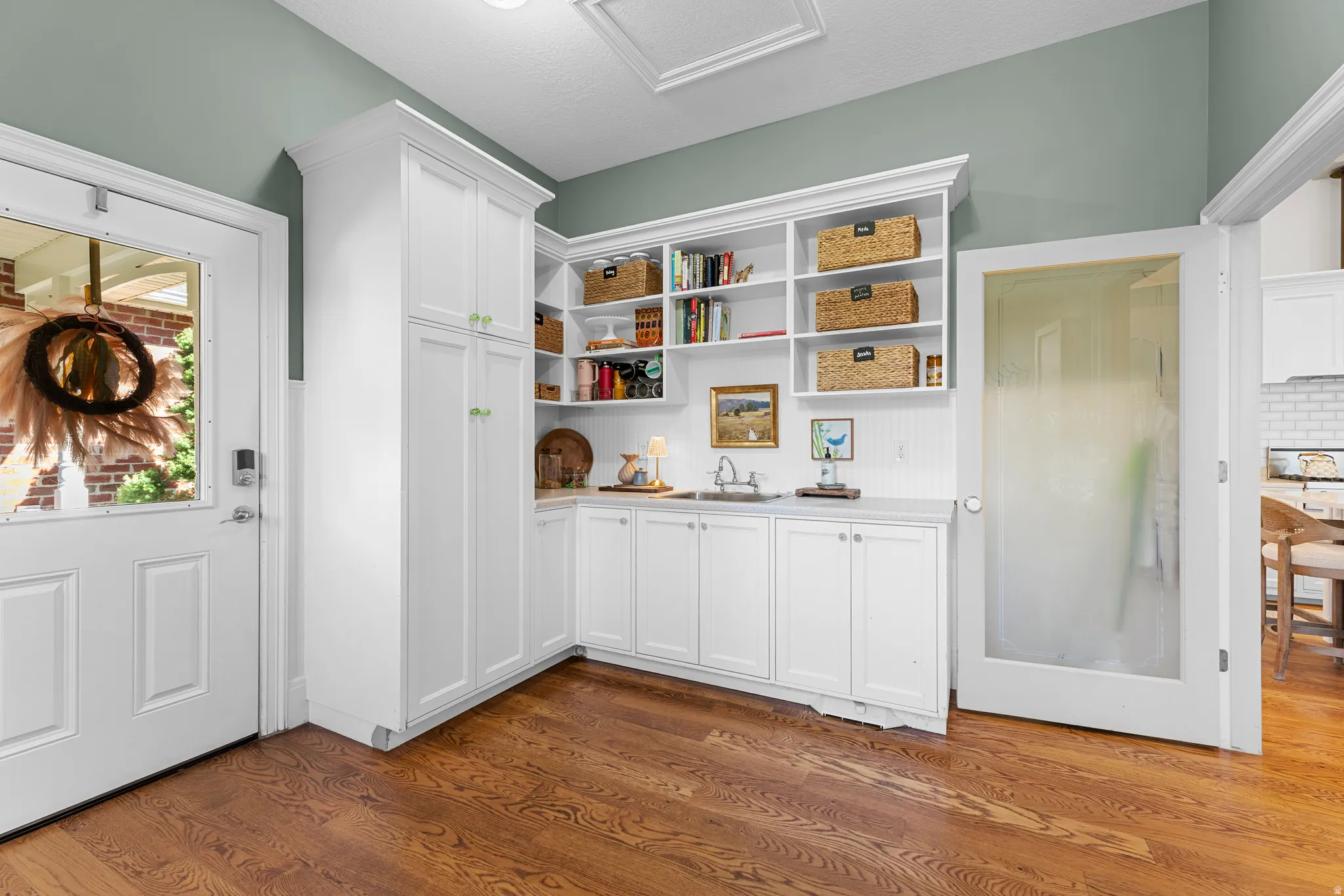 Hardwood flooring, extensive white built-in cabinetry, integrated sink, and open shelving