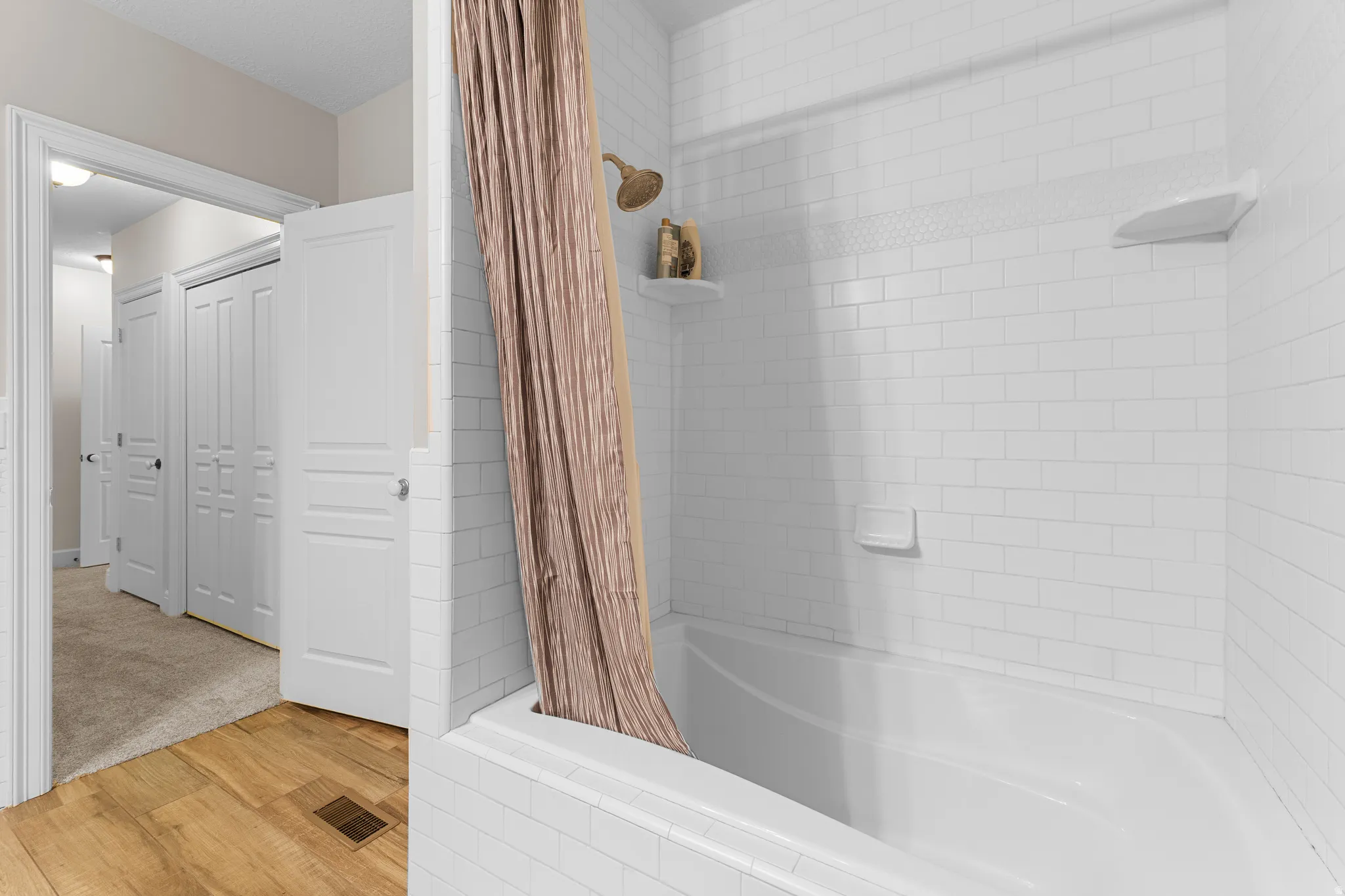 Bathtub with white subway tile surround, integrated shower, and built-in shelving
