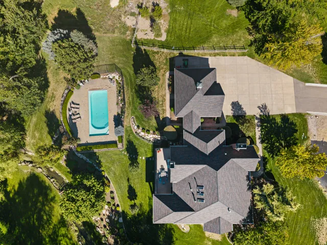 Expansive property featuring a multi-level residence, a rectangular swimming pool with surrounding patio, extensive paved driveway, and mature landscaping