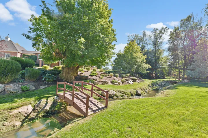 Wood-finish pedestrian bridge over a natural creek, surrounded by mature trees and landscaping