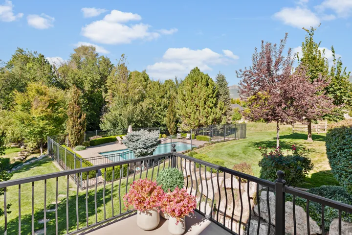 Outdoor swimming pool with surrounding patio, black metal fencing, manicured lawn, and mature trees