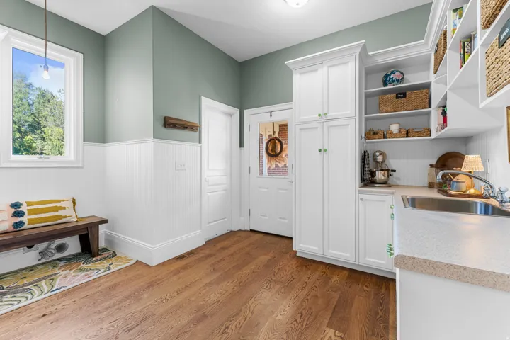 Wood-finish flooring, white beadboard wainscoting, white built-in cabinetry, stainless steel sink, and light-colored countertops