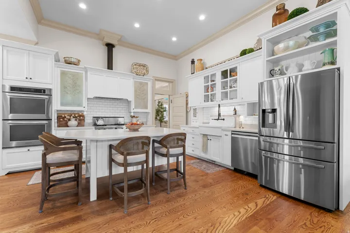 White cabinetry with integrated stainless steel appliances, a central island with a light-colored countertop, wood-finish flooring, a subway tile backsplash, and an apron-front sink