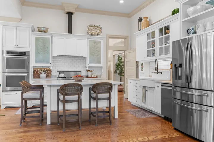 Gleaming wood-finish flooring, white cabinetry, integrated double ovens, a center island, and a farmhouse sink with a black-finish faucet