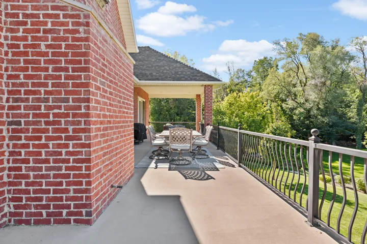 Expansive outdoor patio with a covered section, brick exterior, and decorative wrought iron railing